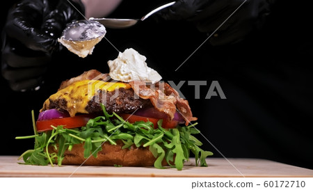 Craft burger is cooking on black background. Consist: sauce, arugula, tomato, onion, bacon, currant sauce, ricotta cheese, air bun and marble meat. 60172710