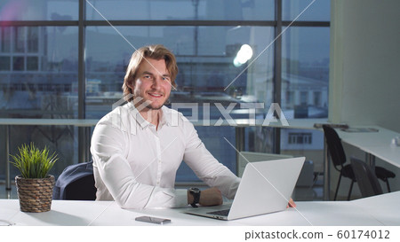 Portrait of modern attractive businessman working at desk in office using laptop 60174012