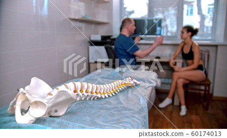 Chiropractic treatment - the doctor inspecting the young woman before the session - model of the human spine placed on the couch in the cabinet Chiropractic treatment - the doctor inspecting the young woman before the session - model of the human spine placed on the couch in the cabinet 60174013