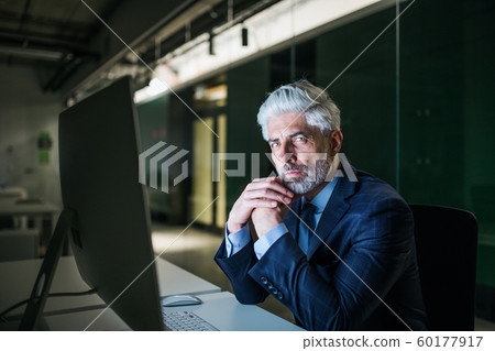 Portrait of mature businessman with computer in an office, looking at camera. Portrait of mature businessman with computer in an office, looking at camera. 60177917