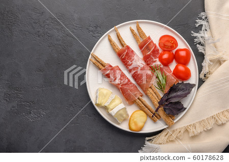 Traditional Italian food is grissini bread with prosciutto, cheese and tomatoes with herbs on a 60178628