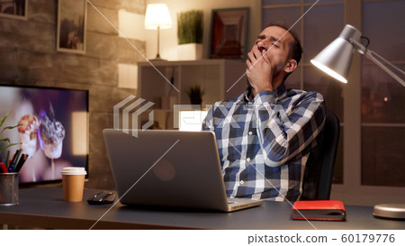 Tired manager yawning while working on laptop Tired manager yawning while working on laptop 60179776