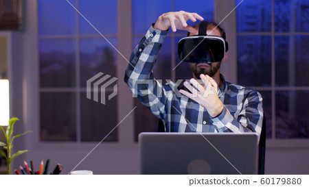 Young businessman using virtual reality goggles at night in his home office 60179880