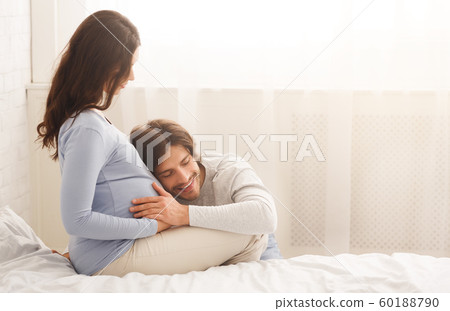 Handsome happy man listening wife's pregnant belly Handsome happy man listening wife's pregnant belly 60188790