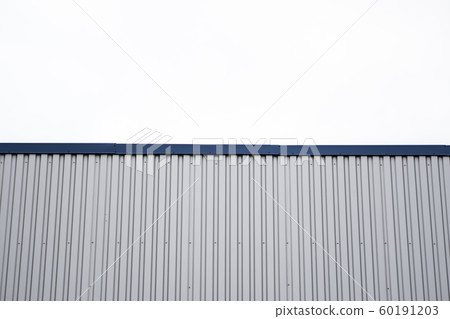 Metal corrugated sheets on a building with a blue metal corners. White aluminium metal corrugated roof or wall sheets against cloudy sky background on a factories and industrial buildings. 60191203