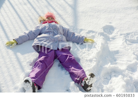 Winter portrait of cheerful child girl having fun in the snow, lying on the snow in the form of angel, top view 60193833