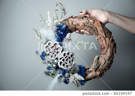Close-up of a florist's hand holding a Christmas wreath with fir branches and cones on the table. Close-up of a florist's hand holding a Christmas wreath with fir branches and cones on the table. 60194547