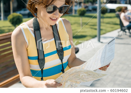 Mature smiling woman with city map and camera, female traveling on a summer sunny day Mature smiling woman with city map and camera, female traveling on a summer sunny day 60194602