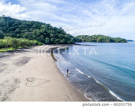Aerial shot of wedding dress couple on the tropical beach Playa Arenillas in Costa Rica with a heart drawn into Sand 60201756