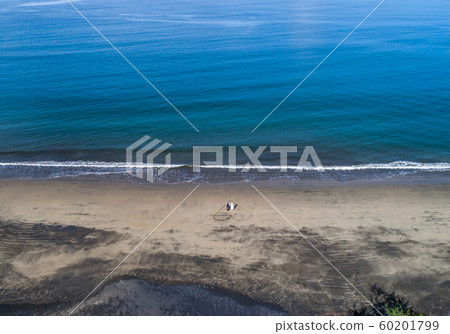 Aerial shot of wedding dress couple on the tropical beach Playa Arenillas in Costa Rica with a heart drawn into Sand 60201799