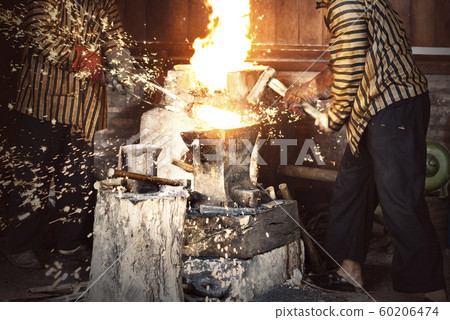 Blacksmith forging the molten metal with a hammer 60206474
