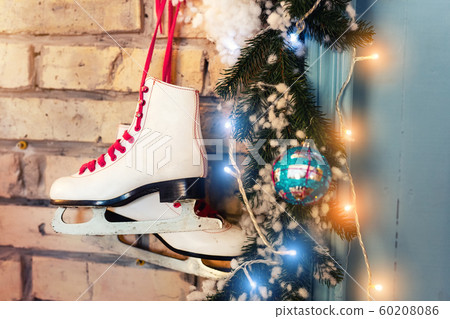 Pair of white vintage leather skates with red laces hanging on old rustic brick wall with glowing garland lights on christmas tree decoration. Cozy scenic christmas card winter holidays background Pair of white vintage leather skates with red laces hanging on old rustic brick wall with glowing garland lights on christmas tree decoration. Cozy scenic christmas card winter holidays background 60208086