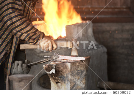 Blacksmith forging the molten metal with a hammer 60209052