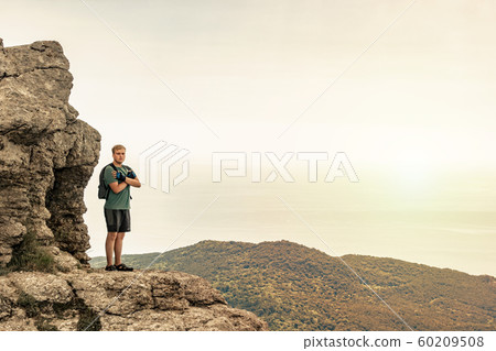 Young man with a backpack on top of cliff enjoying Young man with a backpack on top of cliff enjoying 60209508