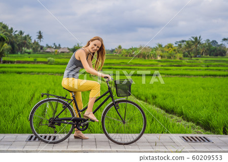 A young woman rides a bicycle on a rice field in Ubud, Bali. Bali Travel Concept 60209553