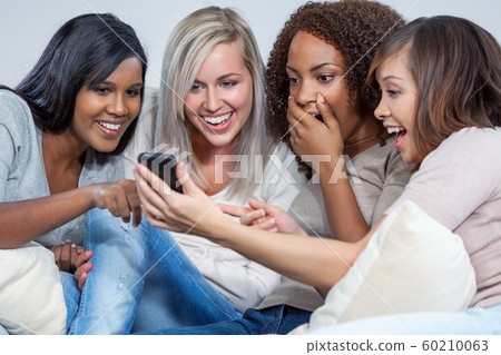 Interracial Group of Female Friends Laughing at Social Media on a Mobile Cell Phone Interracial Group of Female Friends Laughing at Social Media on a Mobile Cell Phone 60210063