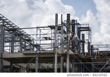 Building and Construction Site in progress. Building construction site against cloudy sky. Metal construction of unfinished building on construction of multi storage building. Building and Construction Site in progress. Building construction site against cloudy sky. Metal construction of unfinished building on construction of multi storage building. 60210382