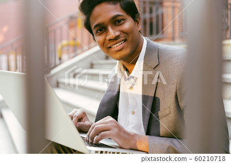 Young handsome Indian man is sitting on the steps Young handsome Indian man is sitting on the steps 60210718