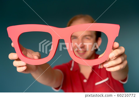 Cheerful man in a red shirt holding big red glasses and looking through 60210772