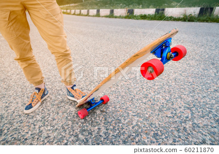 Close-up of male legs in rag sneakers on a longboard on the background of asphalt at sunset. Big skateboard with man legs. Youth leisure concept 60211870