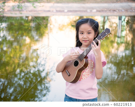 Little asian child girl play the ukulele, in the 60221913