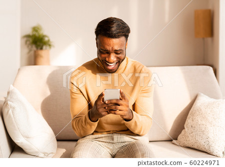 Afro Guy Using Cellphone Playing Games Sitting On Couch Indoor Afro Guy Using Cellphone Playing Games Sitting On Couch Indoor 60224971