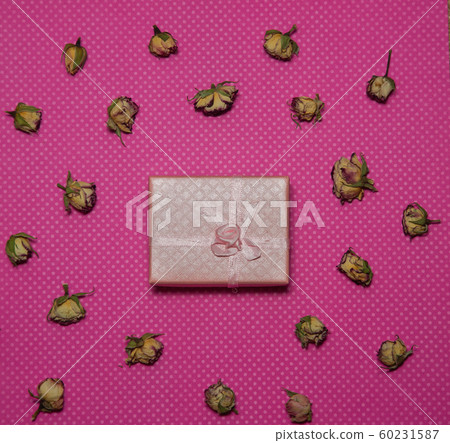 Photo flat lay gift box with bow among dried rose buds on a pink background top view 60231587