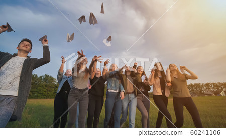 Happy friends launch paper airplanes at sunset. Happy friends launch paper airplanes at sunset. 60241106