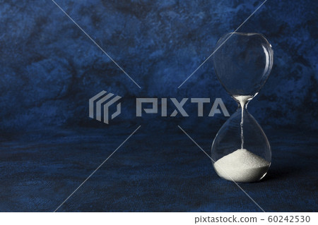 Time is running out concept. An hourglass with oozing sand, on a dark blue background with copyspace 60242530