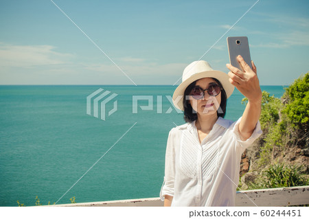 Asian woman standing relax on cliff nearly seashore, She taking selfie with smartphone. 60244451