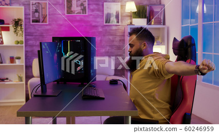 Bearded man sitting on gaming chair stretching while playing video games Bearded man sitting on gaming chair stretching while playing video games 60246959