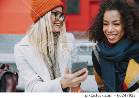 Young Caucasian and Afro American girls looking at smartphone display 60247922