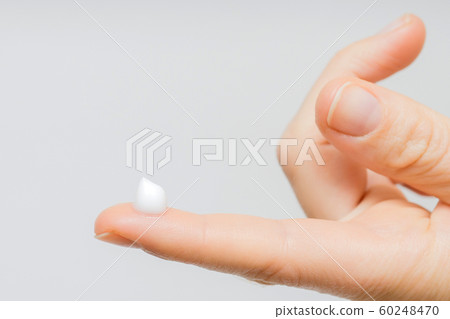 drop of moisturizing cream on fingertip. young girl or adult woman wearing hand cream. woman dropping collagen moisturizer serum into her finger. light background. soft picture 60248470