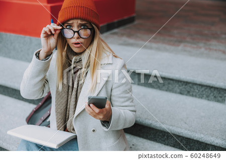 Female student with shocked face looking on smartphone Female student with shocked face looking on smartphone 60248649