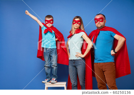 Mom and dad, children superheroes in red cloaks on blank blue background Mom and dad, children superheroes in red cloaks on blank blue background 60250136
