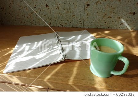 一杯咖啡和一杯咖啡和一個空白的筆記本，在透過窗簾的桌子上的筆記本 60252322