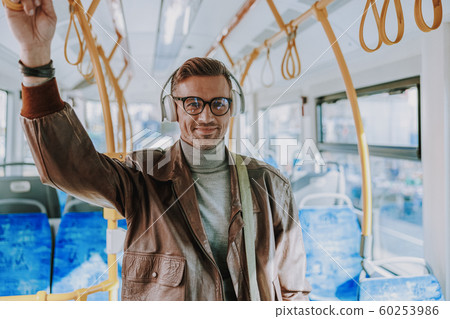 Handsome joyful man listening to music in public transport Handsome joyful man listening to music in public transport 60253986