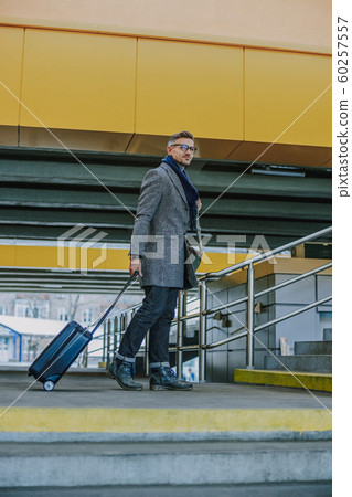 Handsome young man carrying travel suitcase and smiling 60257557