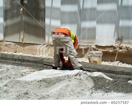 Construction workers creating concrete road curb at the construction site. They are using the in-situ method using the standard metal mold.  60257587