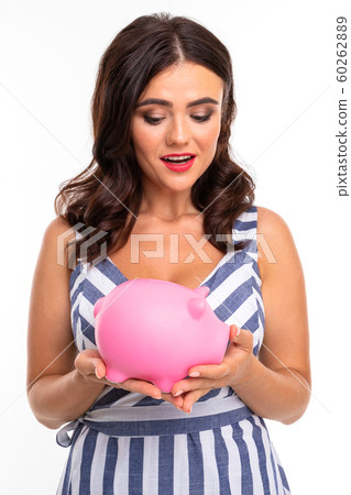 European attractive brunette in dress holds a piggy bank in her hands on a white studio background European attractive brunette in dress holds a piggy bank in her hands on a white studio background 60262889