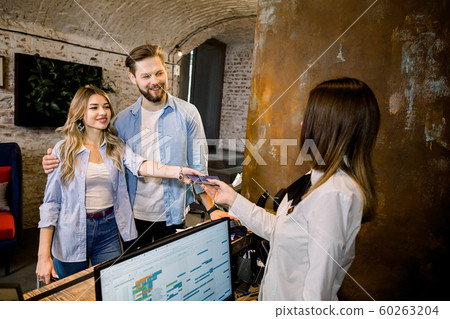 Happy smiling couple giving their reservation details and passports to a concierge while checking in together at the reception counter of a hotel 60263204
