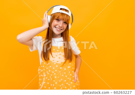 smiling red-haired girl listens to music on headphones on a yellow background. smiling red-haired girl listens to music on headphones on a yellow background. 60263227