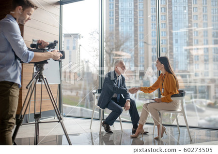 Team of reporters working on a interview with a grey-haired man 60273505