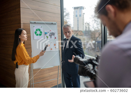 Dark-haired female reporter standing near the white board 60273602