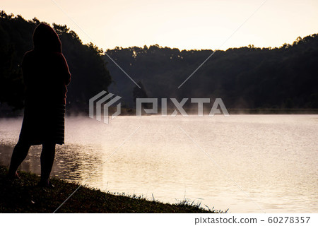 The image behind Woman standing on the lawn And mist floating over the water at Pang Tong reservoir. 60278357