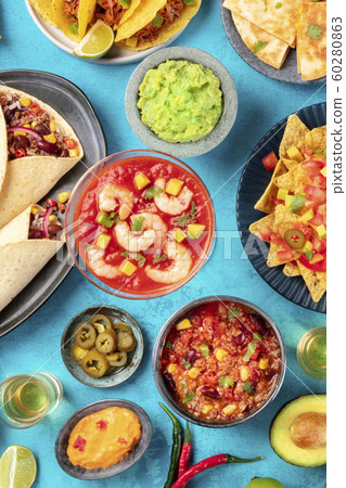 Mexican food, overhead flatlay shot on a vibrant blue background. Shrimp cocktail, chili con carne, guacamole and other dishes Mexican food, overhead flatlay shot on a vibrant blue background. Shrimp cocktail, chili con carne, guacamole and other dishes 60280863
