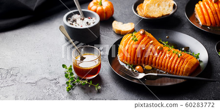 Roasted pumpkin with honey sauce and herbs on a black plate. Slate background. Copy space. 60283772