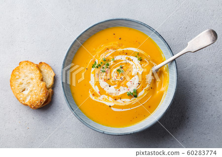 Pumpkin and carrot soup with cream on grey stone background. Top view. Pumpkin and carrot soup with cream on grey stone background. Top view. 60283774