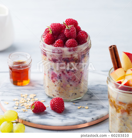 Overnight oats, bircher muesli with raspberry, apple in glass jars on wooden background. Close up. 60283810