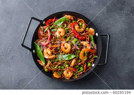 Stir fry noodles with vegetables and shrimps in black pan. Slate background. Top view. Stir fry noodles with vegetables and shrimps in black pan. Slate background. Top view. 60285194